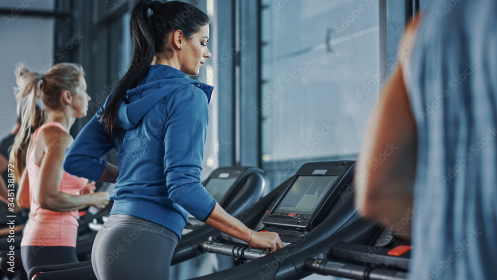 Fit Athletic Woman Running on the Treadmill, Doing Her Fitness Exercise. Muscular Women and Men Acti