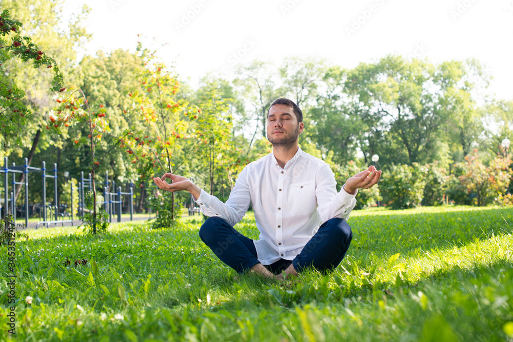 Young man meditates in lotus pose on green grass