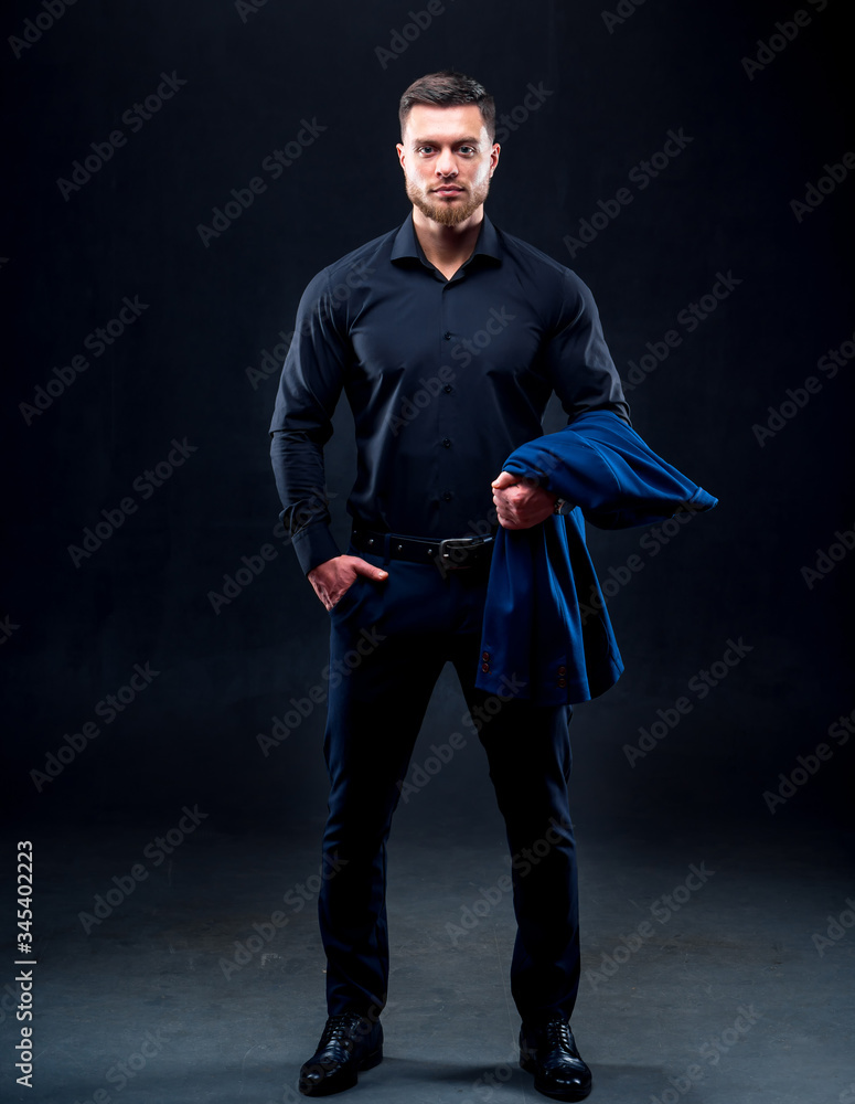 Portrait of handsome young successful man wearing dark shirt. Man holding dark blue jacket. Black ba