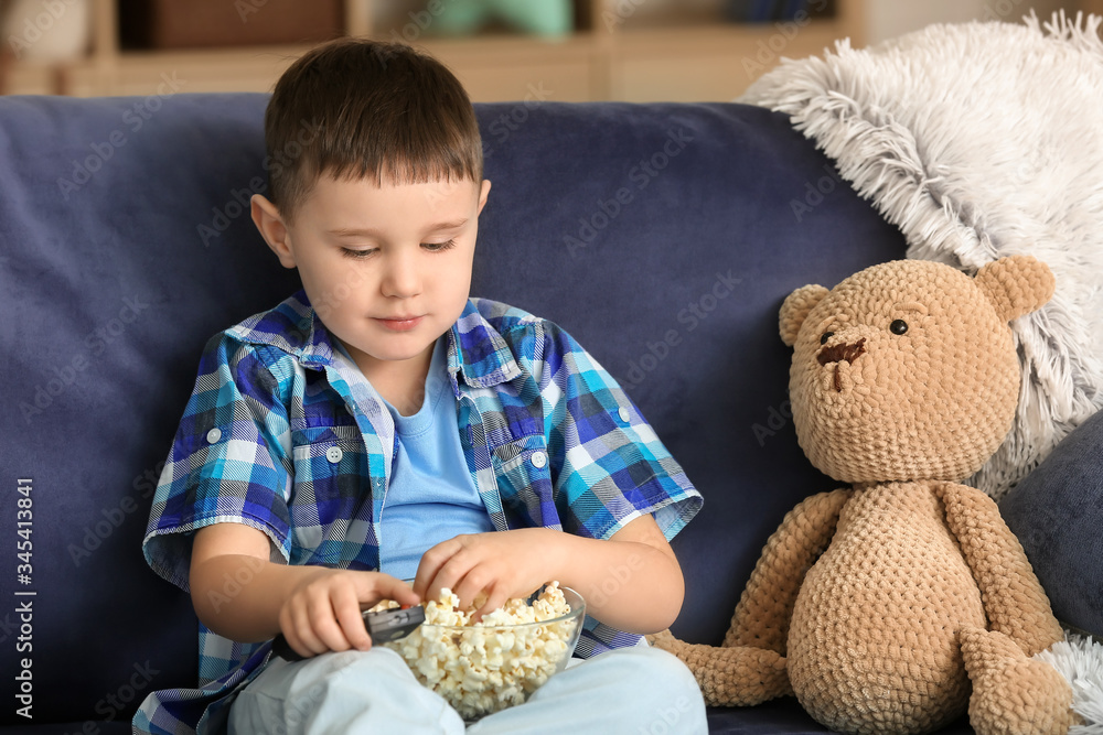 Cute little boy eating popcorn and watching TV at home