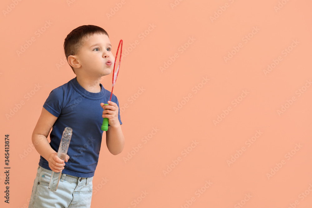 Cute little boy blowing soap bubbles on color background