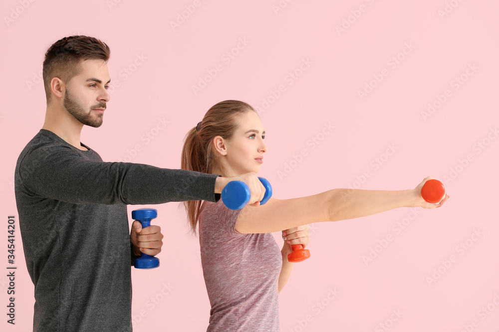 Sporty young couple training with dumbbells on color background