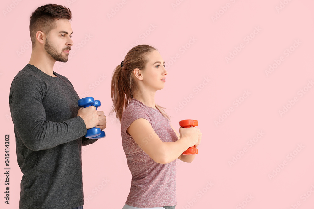 Sporty young couple training with dumbbells on color background