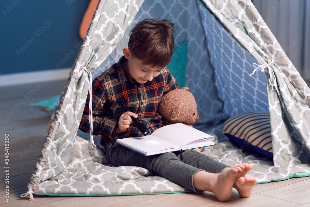 Little boy reading book in play tent at night