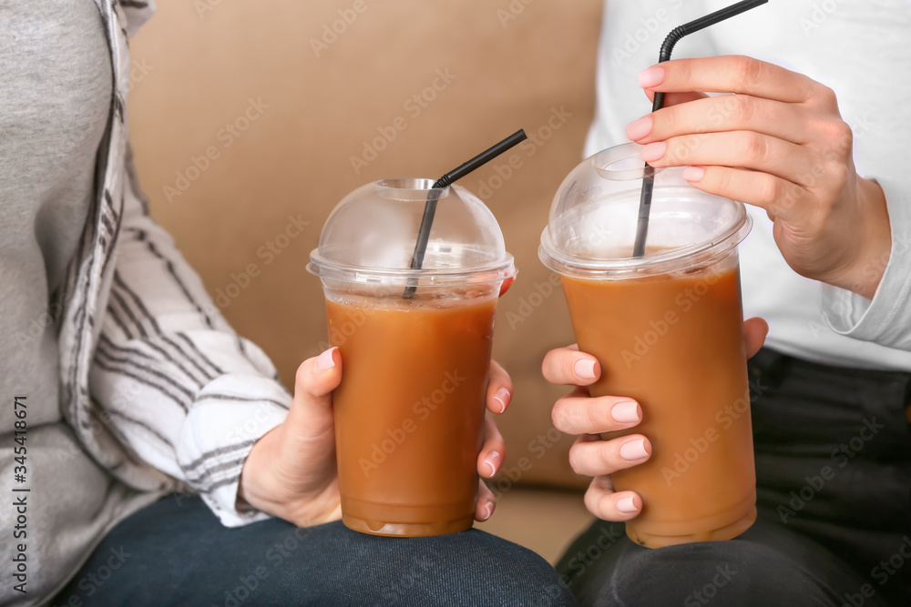 Women with cups of tasty iced coffee in cafe, closeup