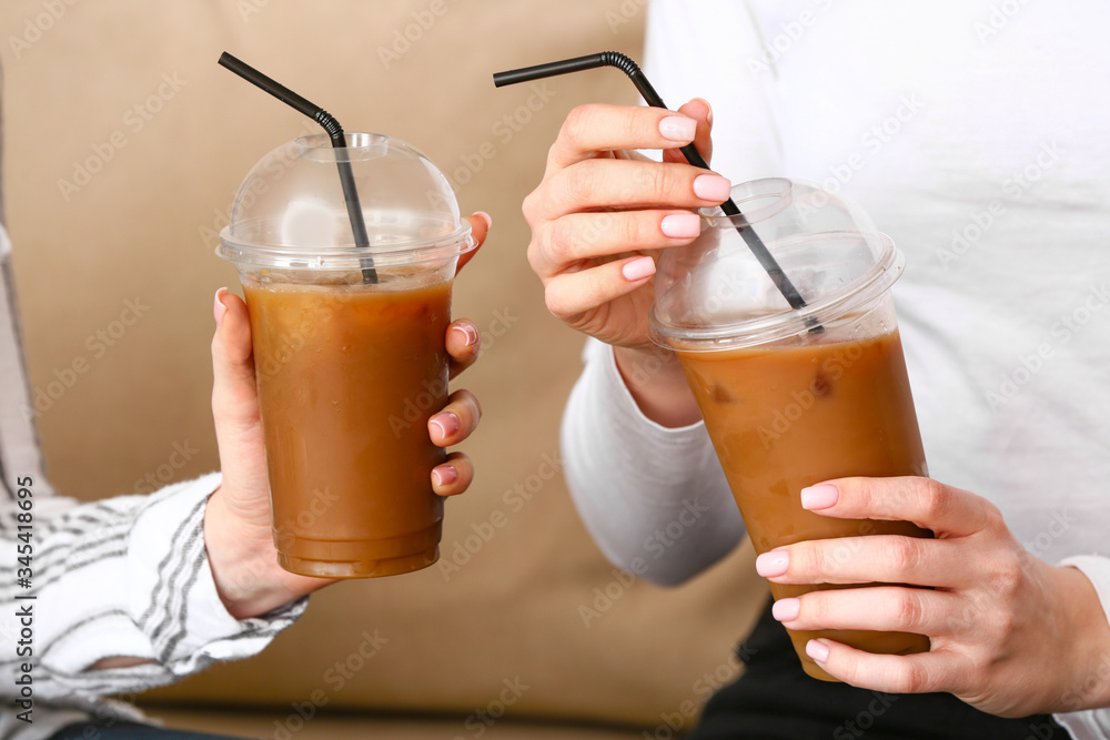 Women with cups of tasty iced coffee in cafe, closeup