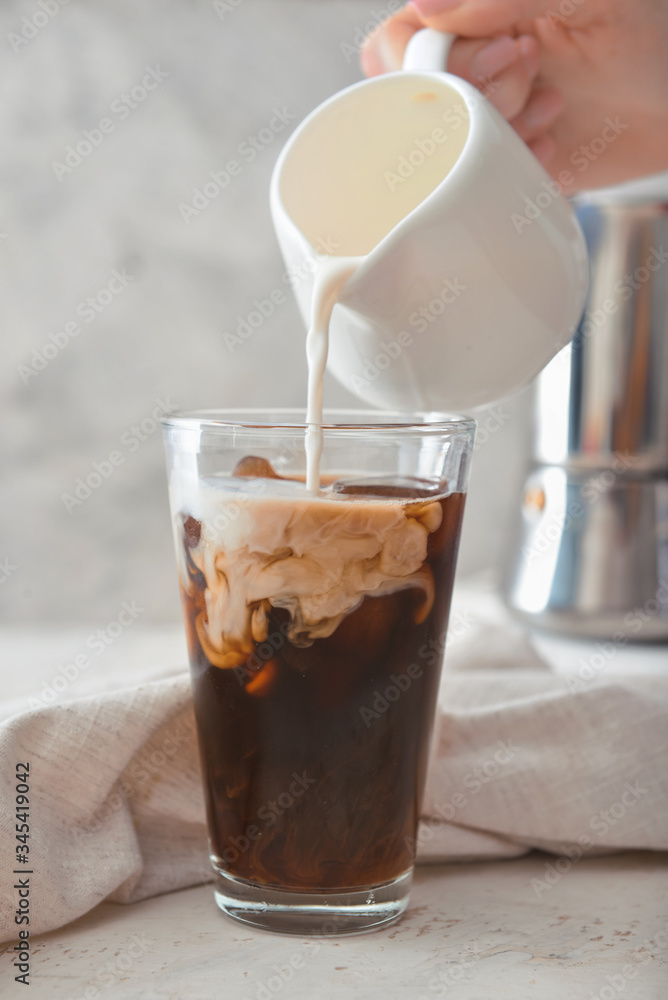 Pouring of milk into cold coffee in glass on table