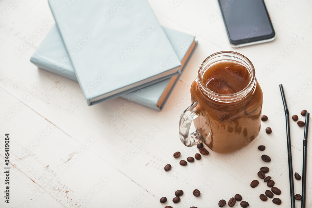 Mason jar of tasty iced coffee with notebooks and mobile phone on table