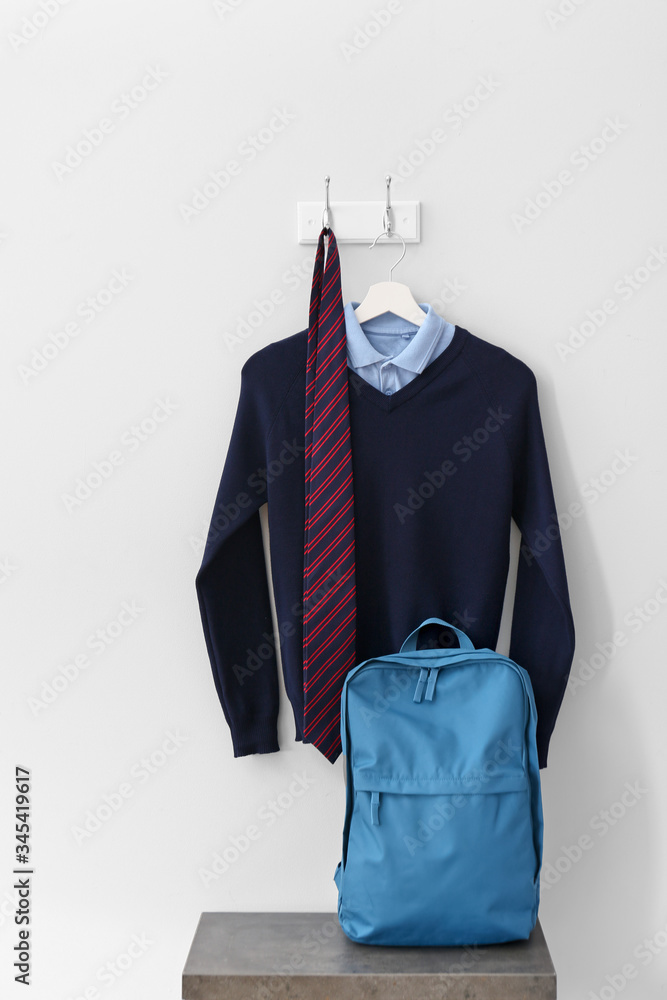 Stylish school uniform with backpack in room