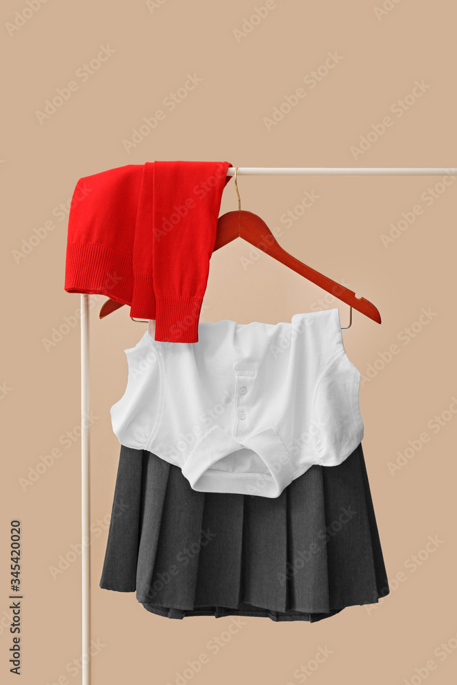 Stylish school uniform hanging on rack against color background