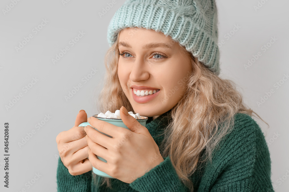 Beautiful young woman with cup of hot chocolate on grey background