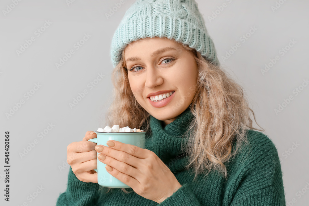 Beautiful young woman with cup of hot chocolate on grey background