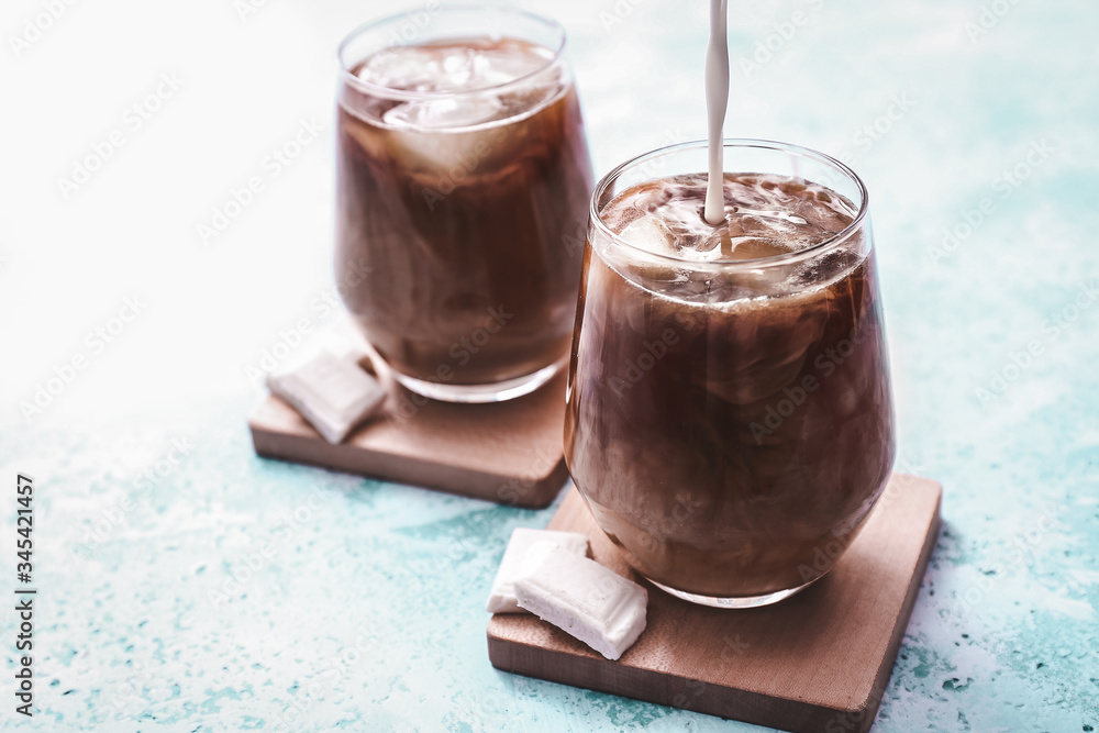 Pouring of milk into cold coffee in glass on color background