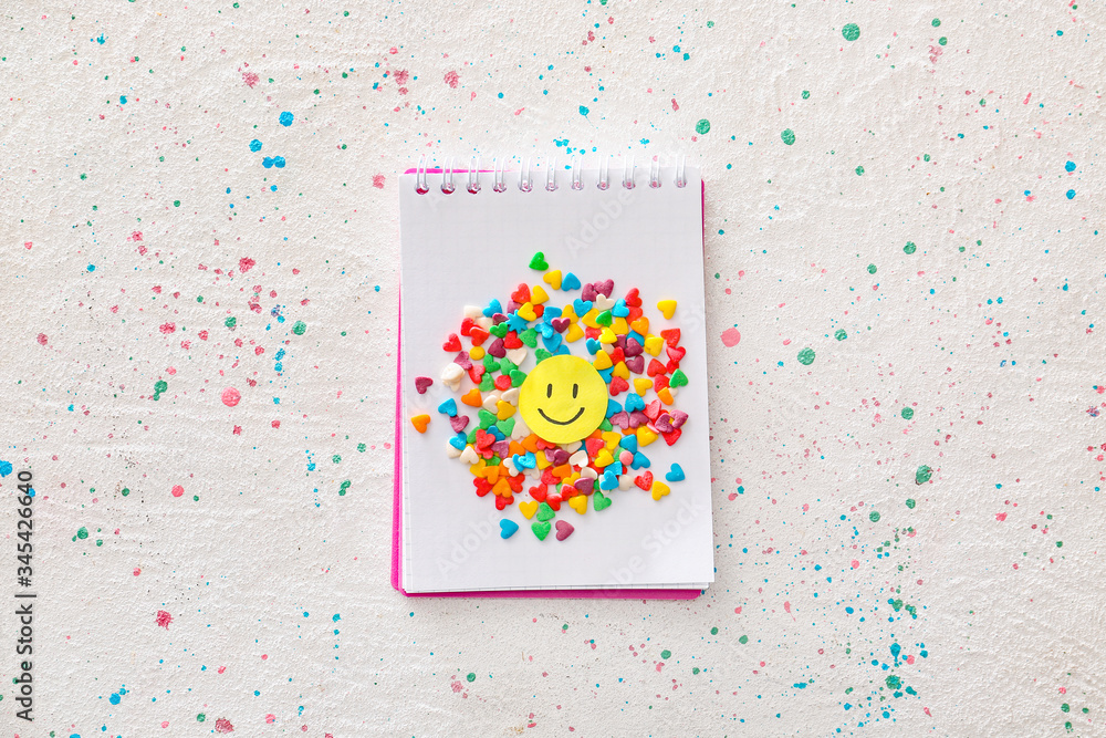 Notebook with sprinkles and paper smile on light background