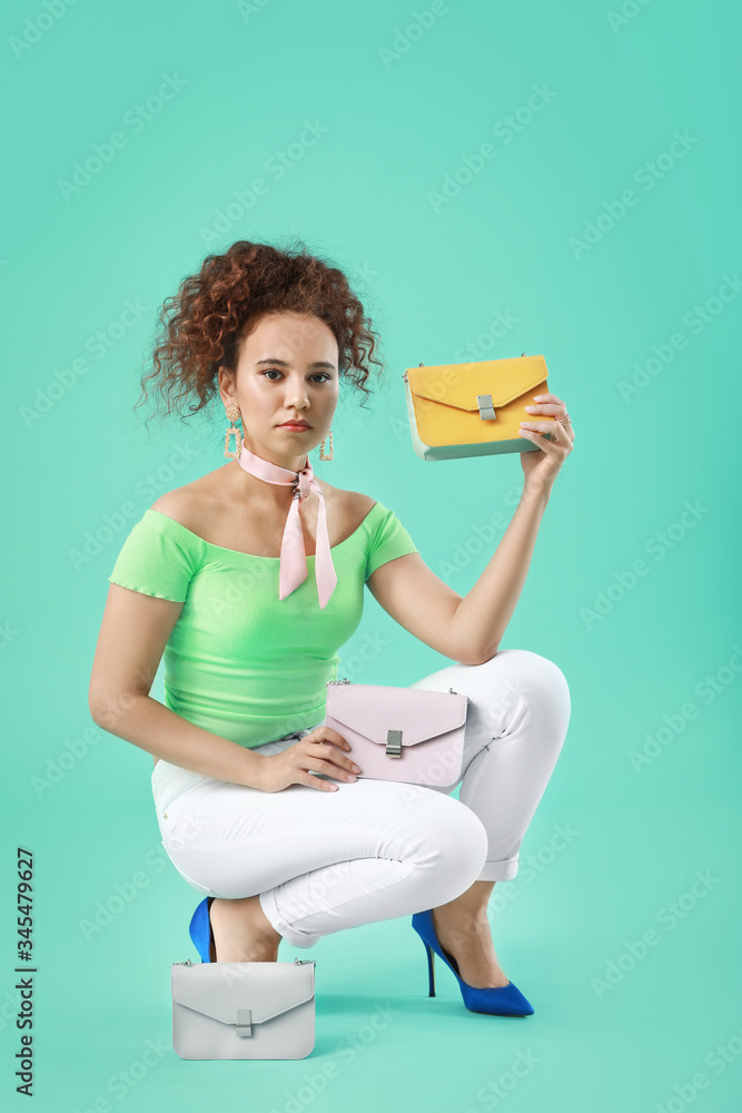 Beautiful young African-American woman with stylish bags on color background