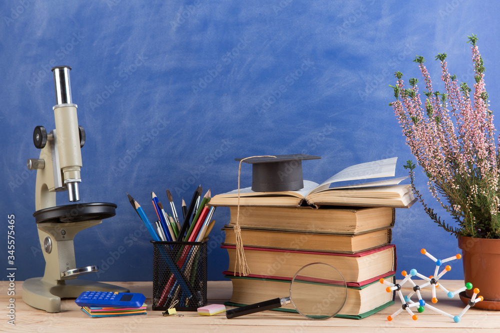 Education and sciences concept - books on the teacher desk in the auditorium, chalkboard on the back