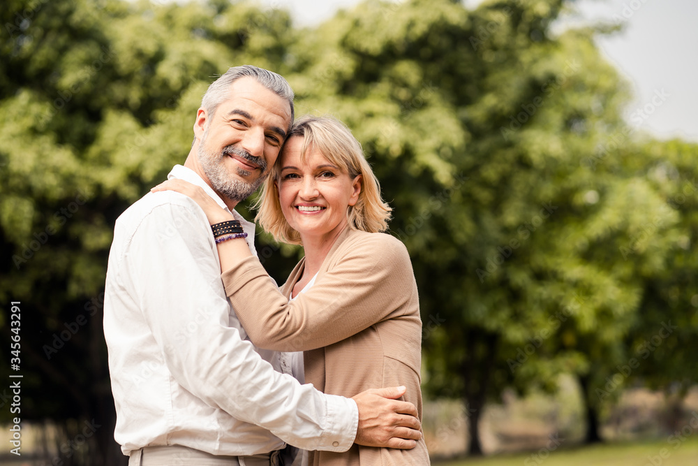 Senior elder Caucasian couple sitting on ground together in park in Autumn. Wife hugging husband fro