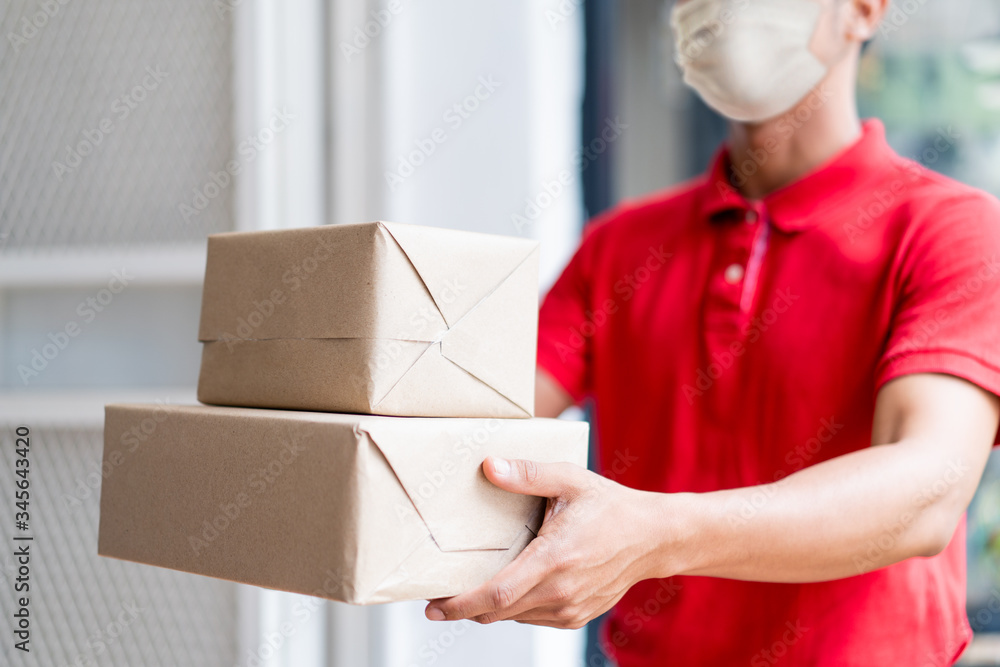 Asian postman, deliveryman wearing mask carry small box deliver to customer in front of door at home