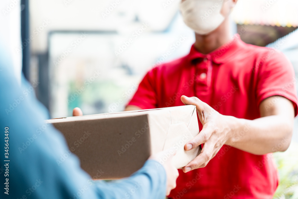 Asian postman, deliveryman wearing mask carry small box deliver to customer in front of door at home