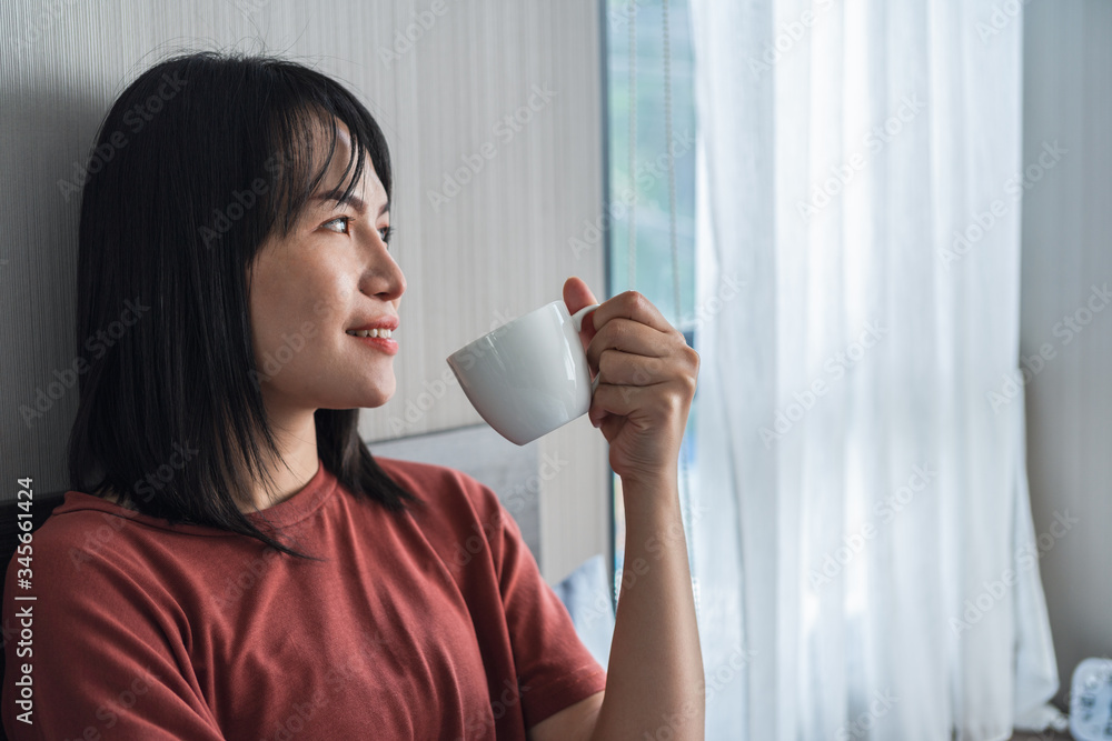 女人在卧室里用手拿着一杯咖啡，看着窗帘概念复古现代