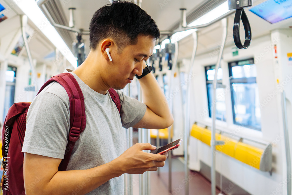 Close up of young man listening to music with wireless earpods and using mobile phone while commutin