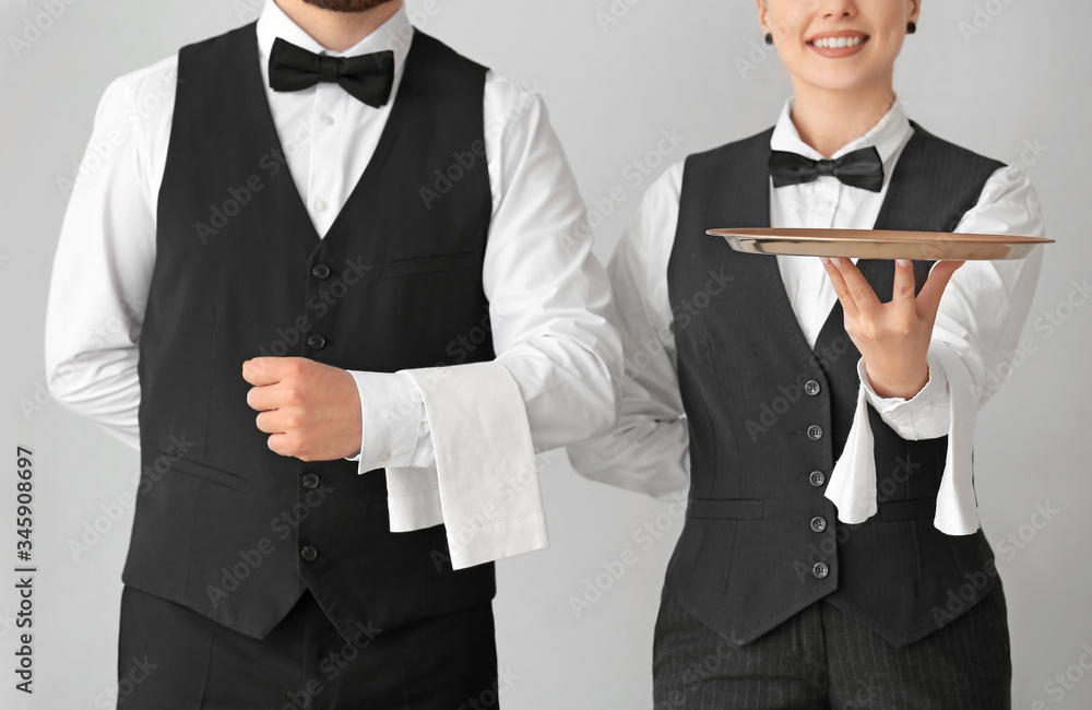 Male and female waiters on grey background