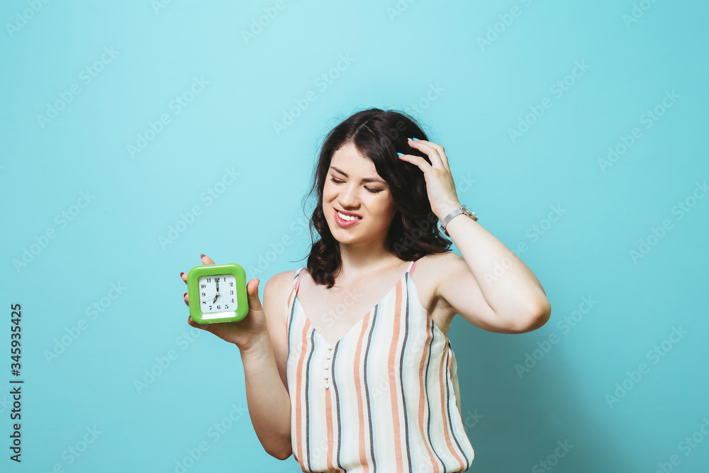 Image of a sad thinking young Asian  woman posing isolated over pink wall background holding clock.