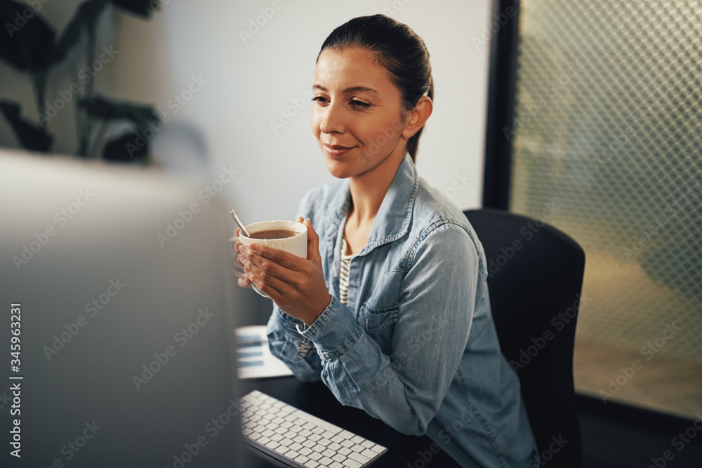 微笑的年轻女商人坐在办公室喝茶