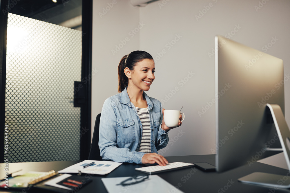 Smiling businesswoman drinking tea while working at her desk