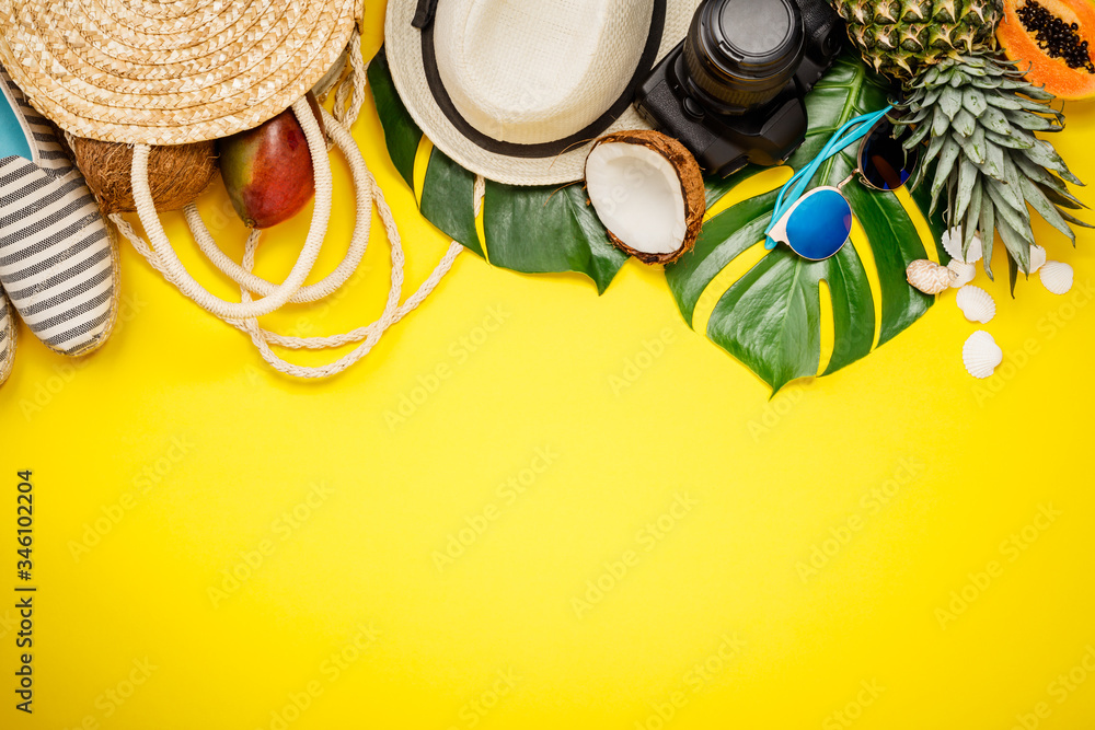 Straw hat, camera, bag, summer shoes, sunglasses, shells, tropical leaves and fruits over yellow bac