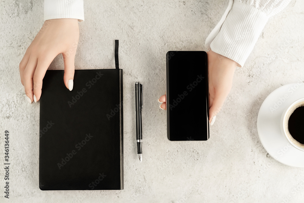 Beautiful womens hands with up-to-date smartphone, notebook, fountain pen and cup of coffee on conc