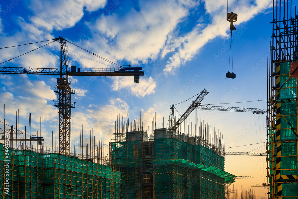 Tower crane and building construction site silhouette at sunrise.