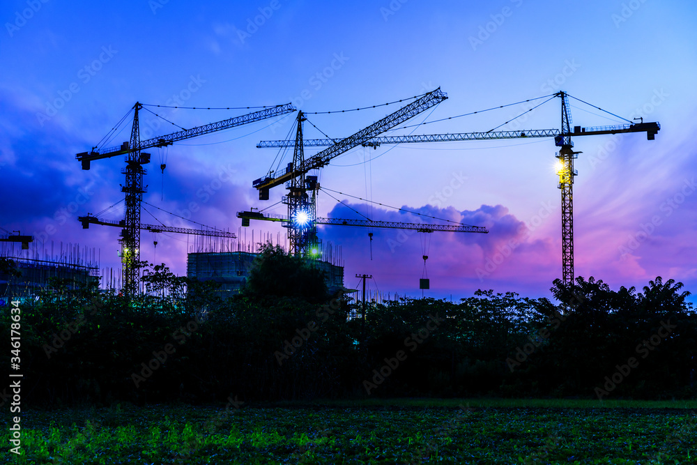 Tower crane and building construction site silhouette at sunrise.