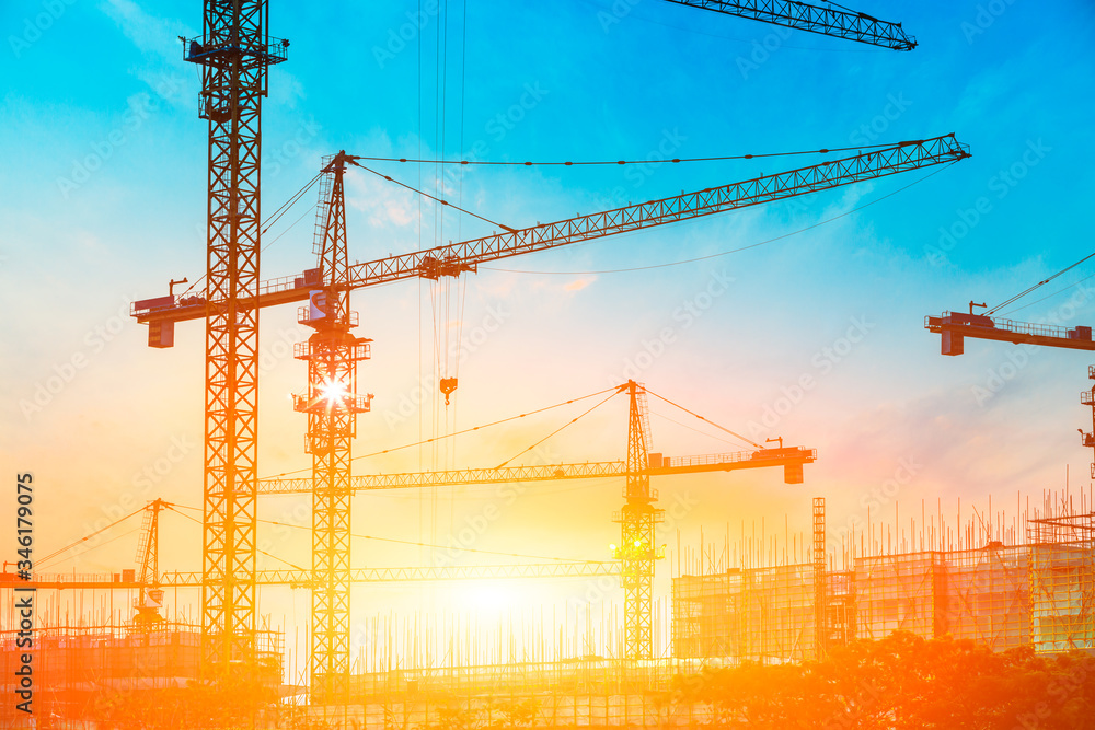 Tower crane and building construction site silhouette at sunrise.