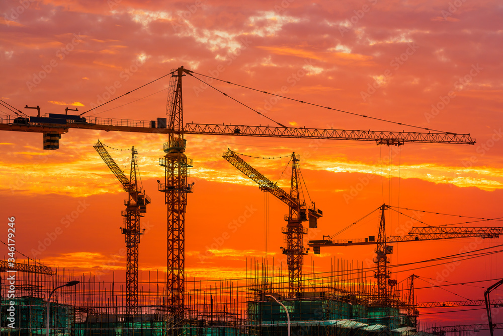 Tower crane and building construction site silhouette at sunrise.