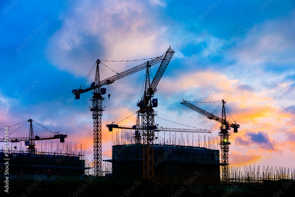 Tower crane and building construction site silhouette at sunrise.