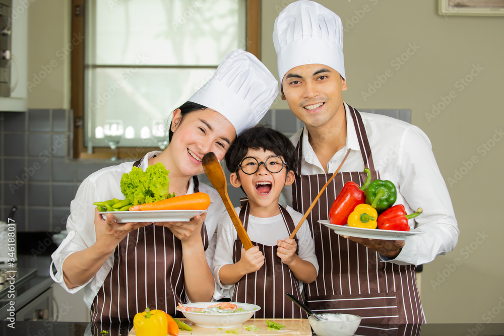 快乐可爱的小男孩，父母戴着帽子，在家里的厨房里烹饪新鲜的沙拉蔬菜