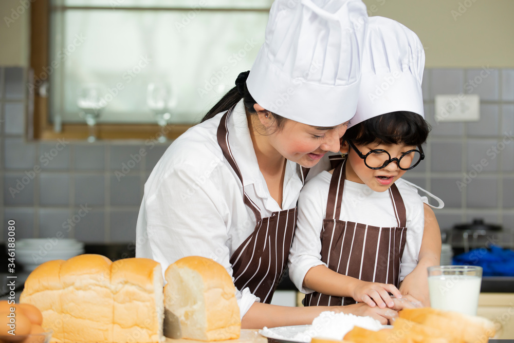 Happy cute asian  little boy with mother in apron chef hat preparing baking the dough in kitchen roo