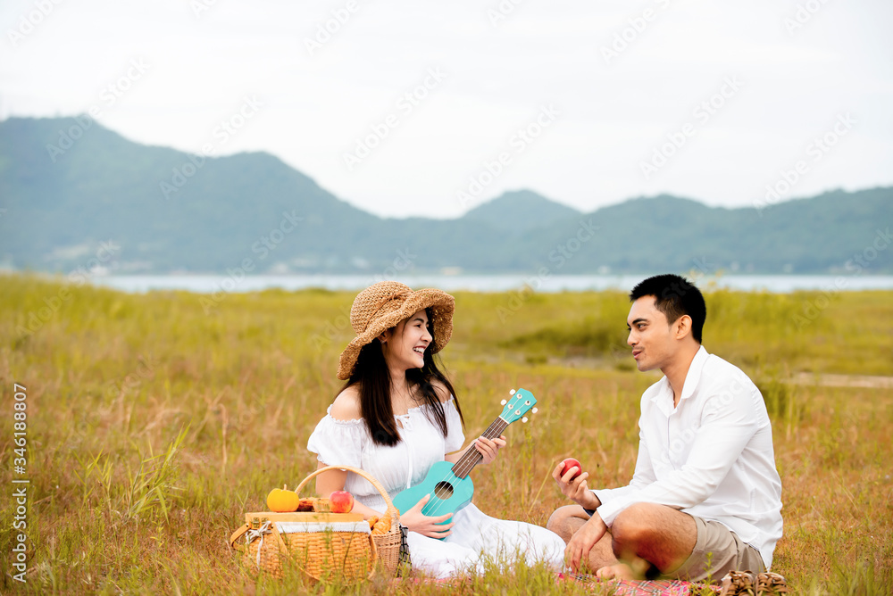 Happy asian couple enjoying  with food and playing ukulele guitar in picnic day at park