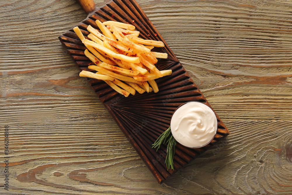 Board with tasty sour cream and french fries on table