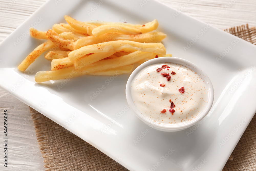 Plate with tasty sour cream and french fries on table