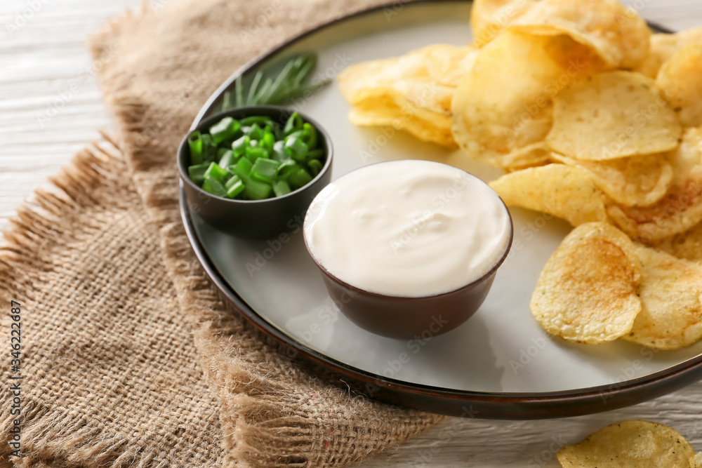 Plate with tasty sour cream, green onion and potato chips on table