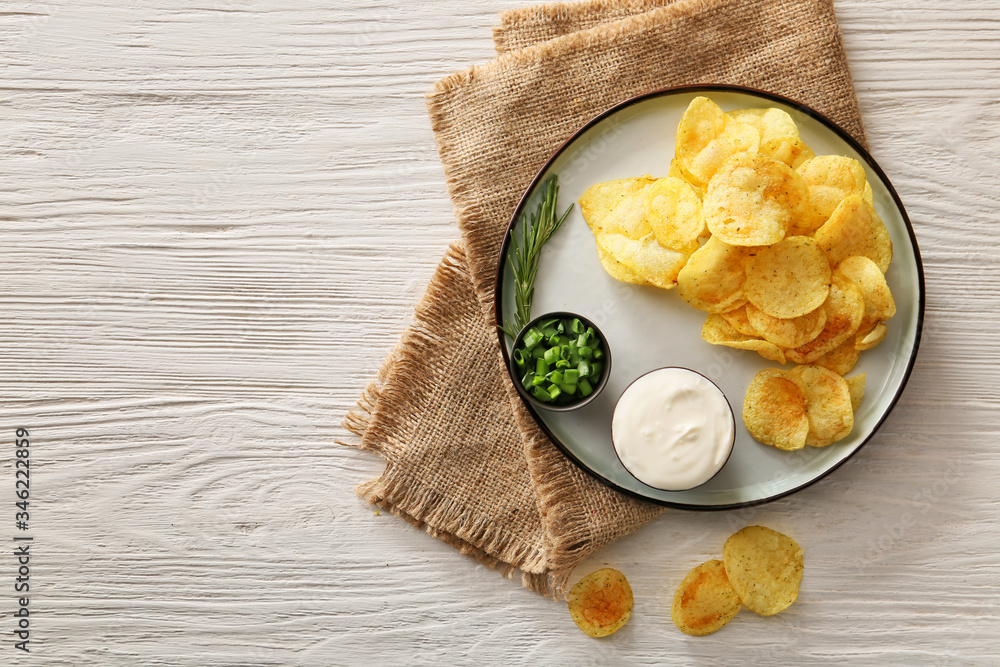 Plate with tasty sour cream, green onion and potato chips on table