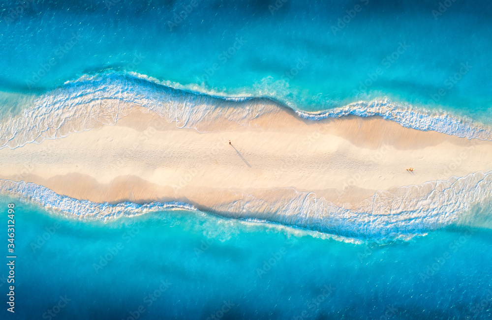 Aerial view of transparent blue sea with waves on the both sides and people on sandy beach at sunset