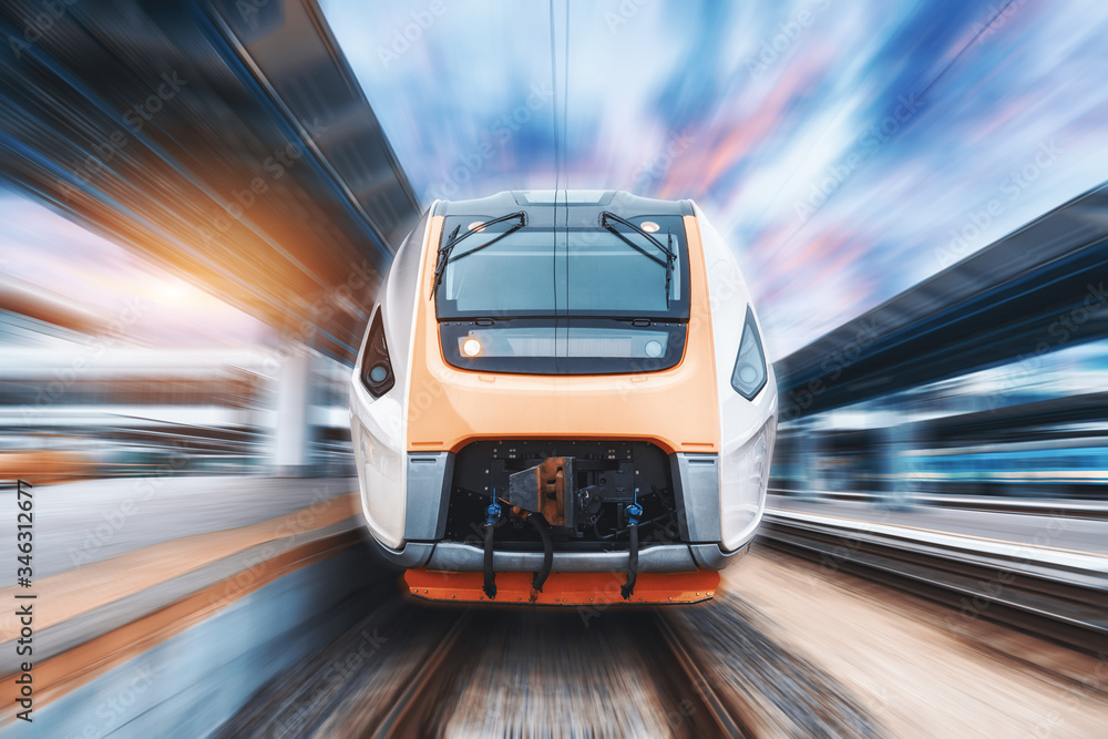 High speed train in motion on the railway station at sunset. Fast moving modern passenger train on t