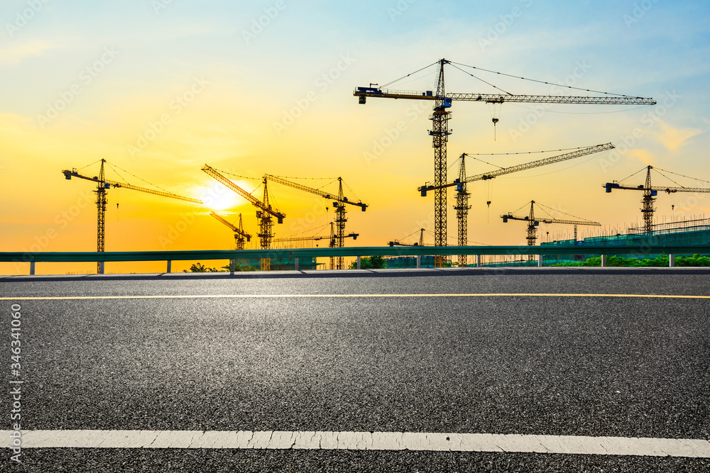 Empty asphalt road and construction site landscape at sunrise.