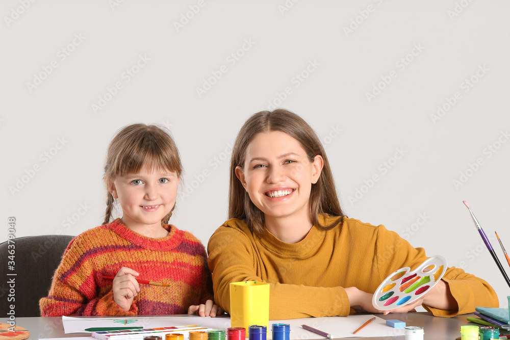 Drawing teacher giving private art lessons to little girl on light background