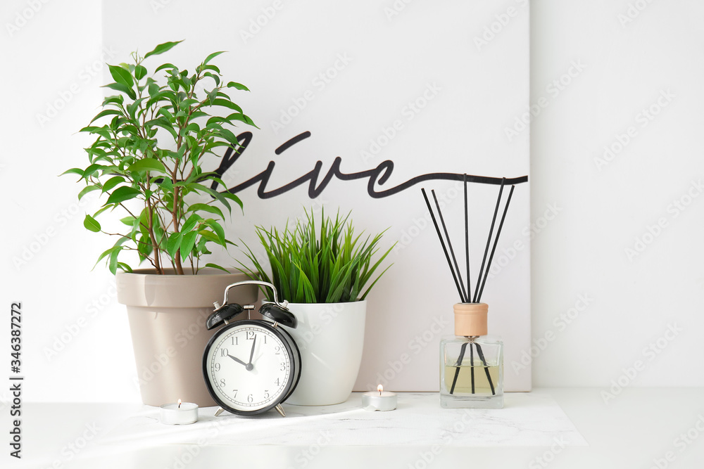 Reed diffuser, clock and houseplants on table in room