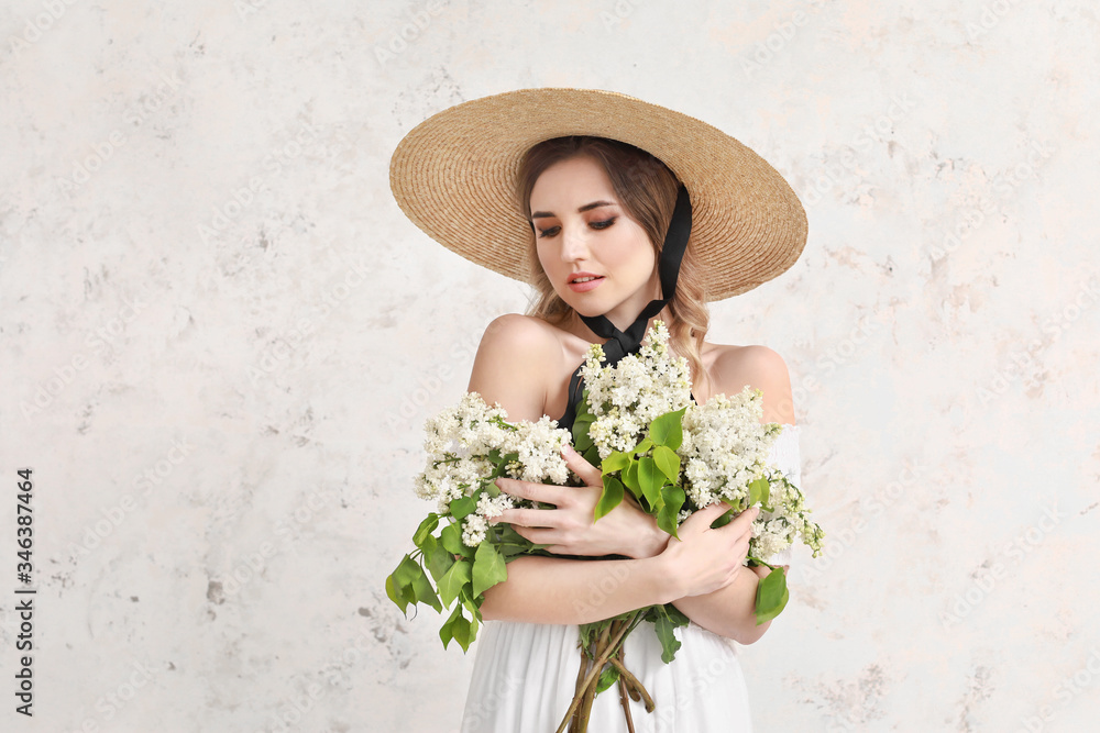 Beautiful young woman with bouquet of lilac flowers on light background