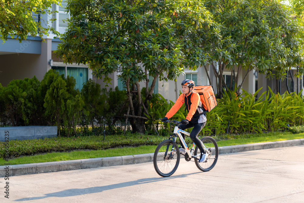 Asian man courier on bicycle delivering food in town streets with a hot food delivery from take away